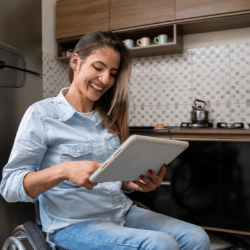 Disabled woman in wheelchair in kitchen using iPad