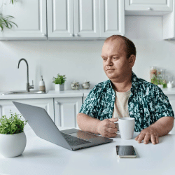 Disabled man sitting at kitchen table using laptop