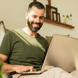 Happy man smiling while using laptop at home