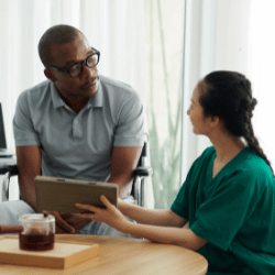 Disabled man in wheelchair talking with nurse at home