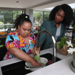 Disabled woman washing vegetables in kitchen with support worker