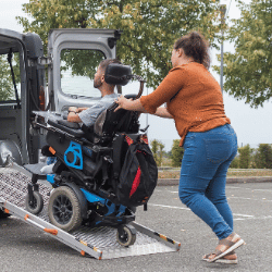 Support worker helping disabled man in wheelchair up ramp into van