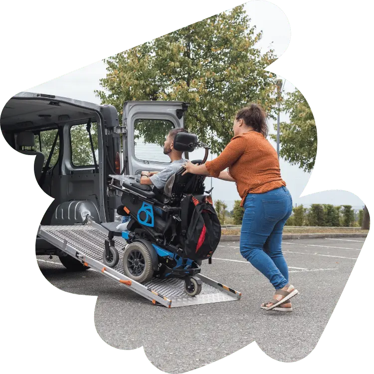 Support worker helping disabled man in wheelchair up ramp into van
