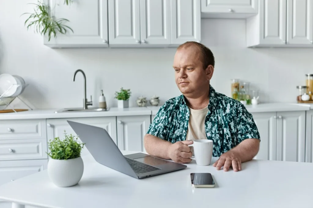 Disabled man sitting at kitchen table using laptop