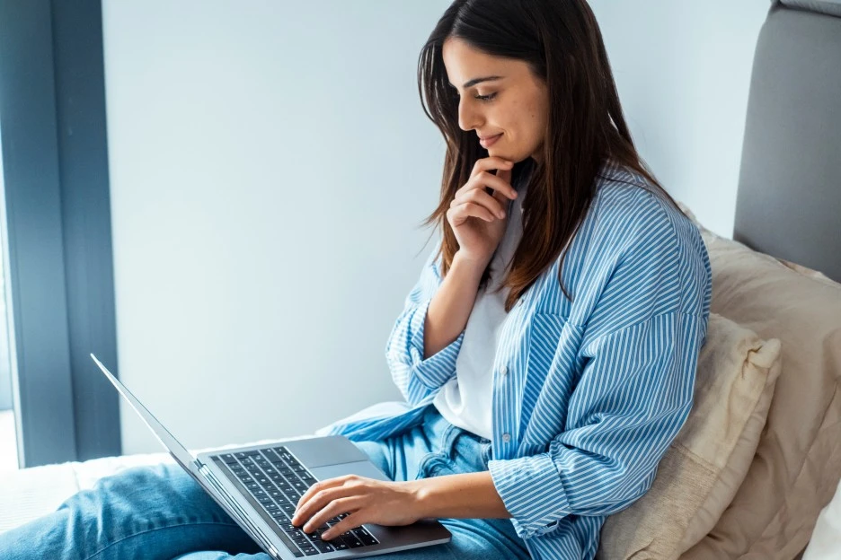 Happy woman sitting down using laptop to look at MCA training