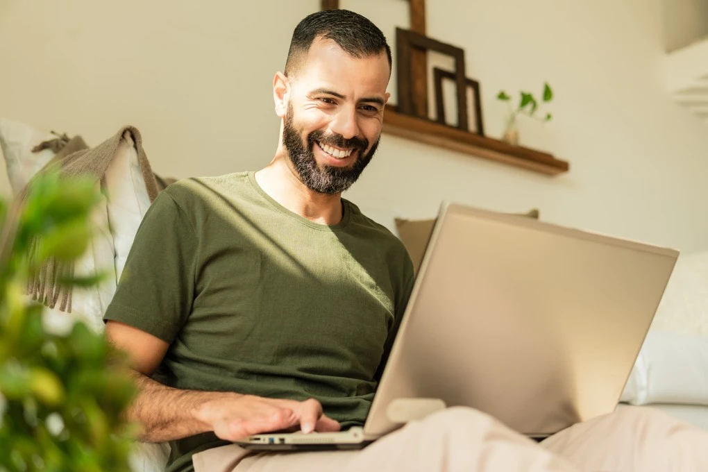 Happy man smiling while using laptop at home