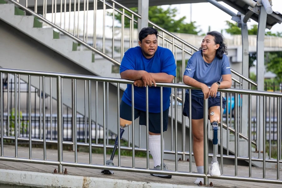 Two quadriplegic disabled friends outside leaning against hand rail while laughing in and talking